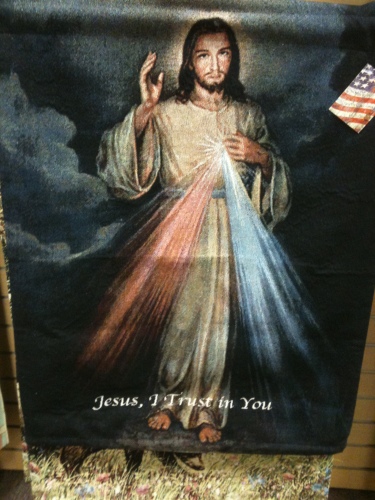 A blanket with a photo of Jesus with red and blue beams of light shining outward from his heart that says "Jesus, I Trust in You" at the bottom